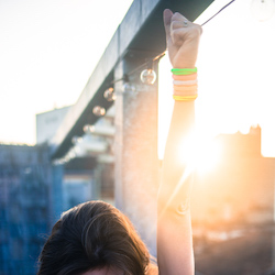 neonica lord wearing luminous bracelets on her arm which is raised in front of the setting sun